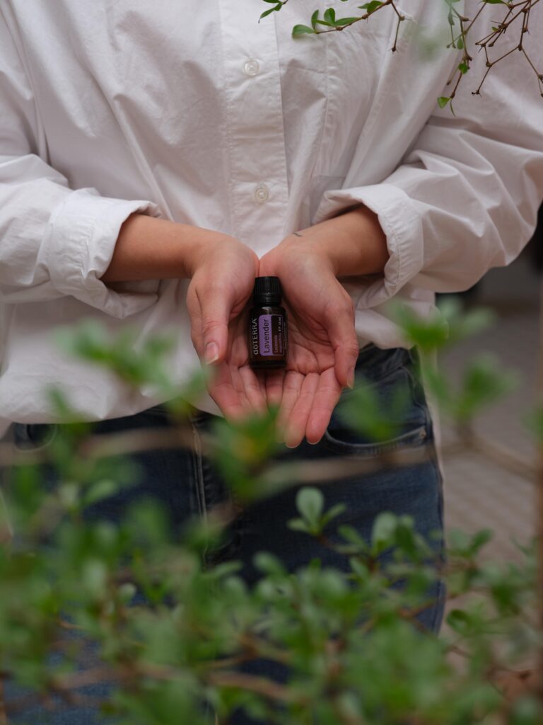 Kobieta trzymająca naturalny olejek eteryczny dōTERRA w dłoniach w otoczeniu zielonych roślin